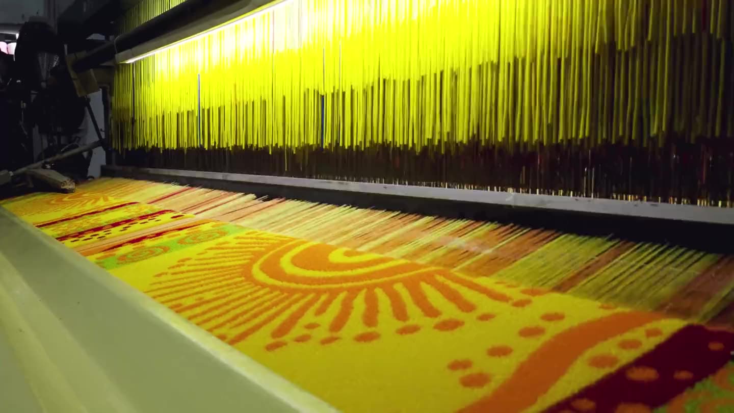 The same sun motif weaving on the loom, the yellow warp running above it.